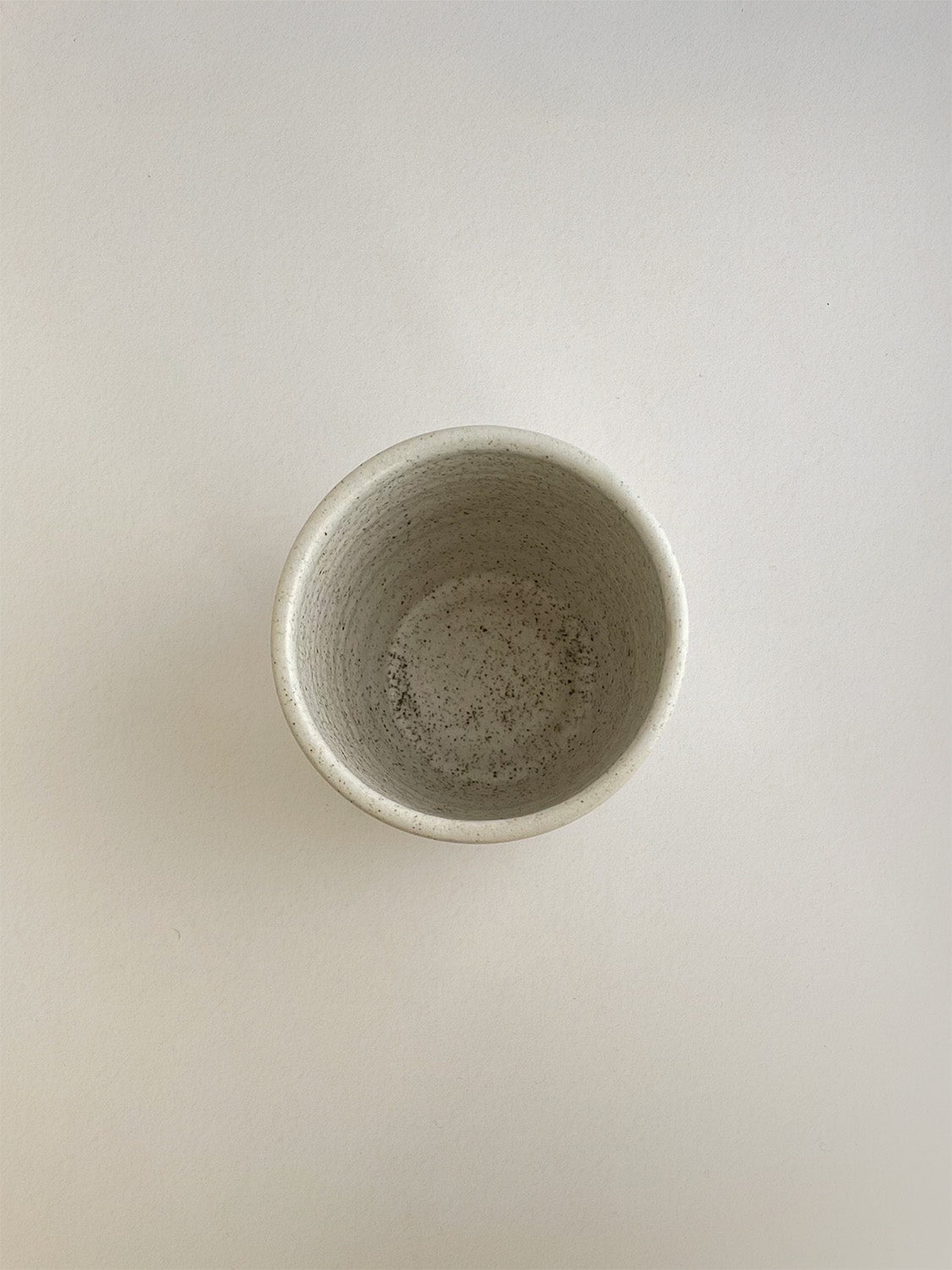 Speckled white ceramic cup on a neutral background - top view.