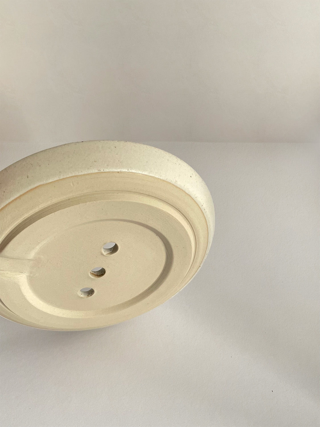 Close-up view of base of ceramic soap dish on a neutral background.