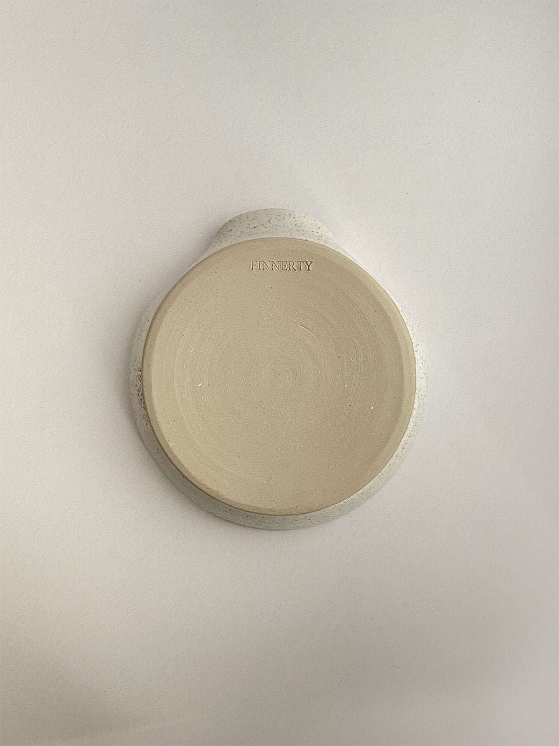 Speckled white ceramic spoon rest on a neutral background - base view.