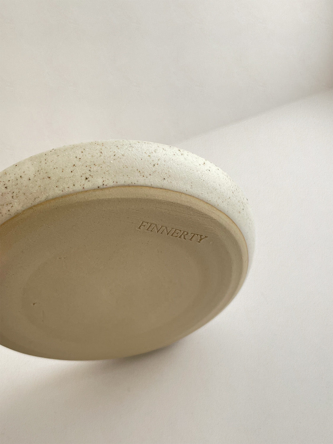 Close-up of speckled white ceramic candle holder on a neutral background.