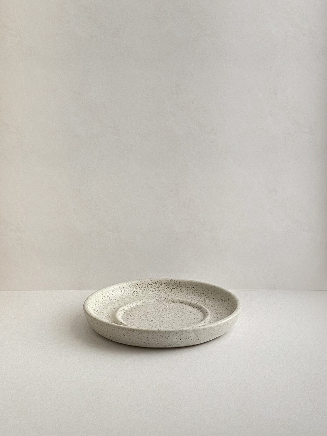 Speckled white ceramic candle holder on a neutral background - front view.