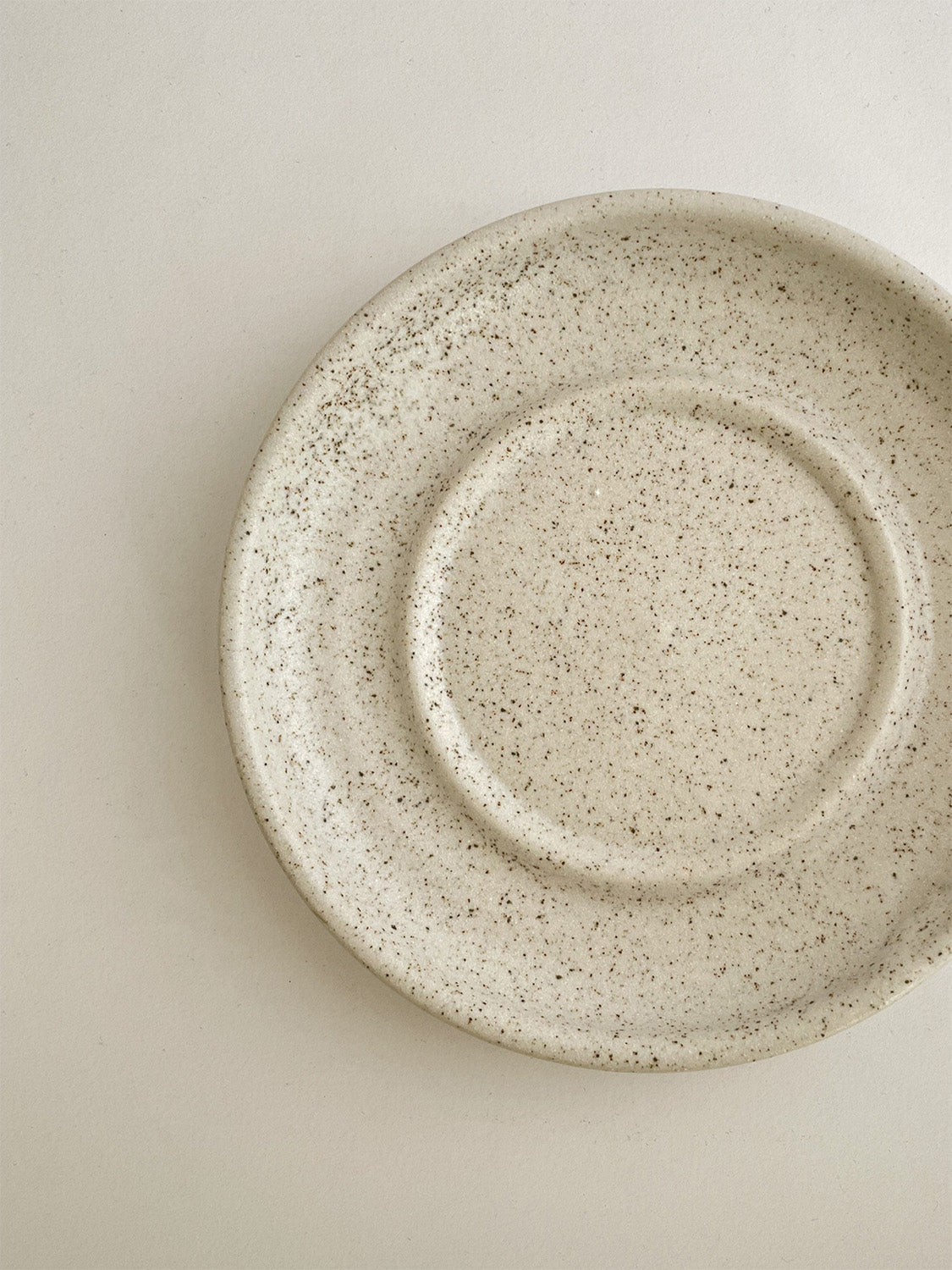 Speckled white ceramic candle holder on a neutral background - top detail.
