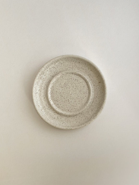 Speckled white ceramic candle holder on a neutral background - top view.