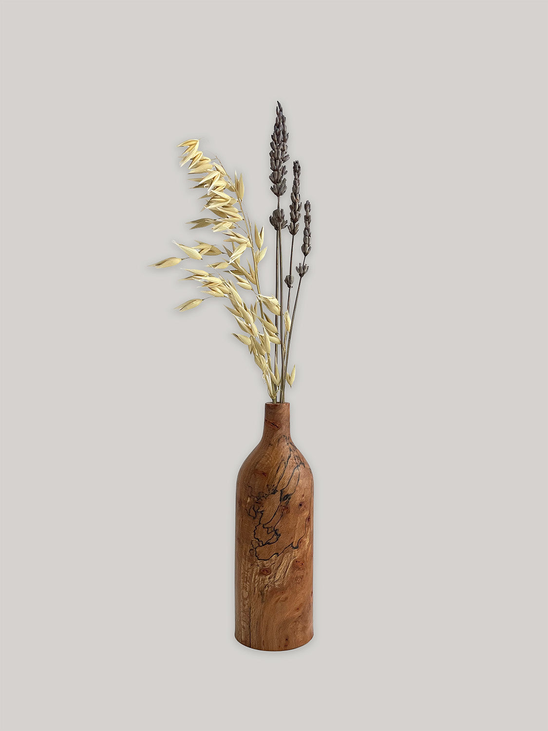 Wooden bud vase with dried flowers on a light grey background.