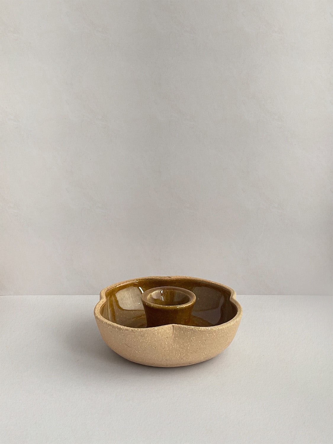 A hand-thrown ceramic candle holder in a rustic yellow ochre glaze on a neutral background - front view.