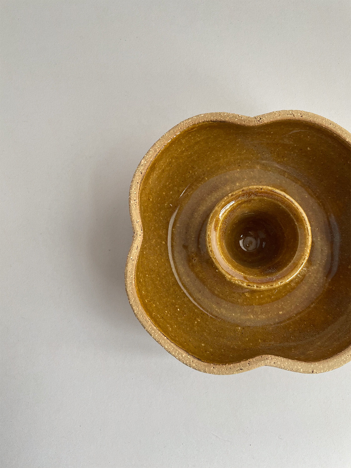A hand-thrown ceramic candle holder in a rustic yellow ochre glaze on a neutral background - top view close-up.