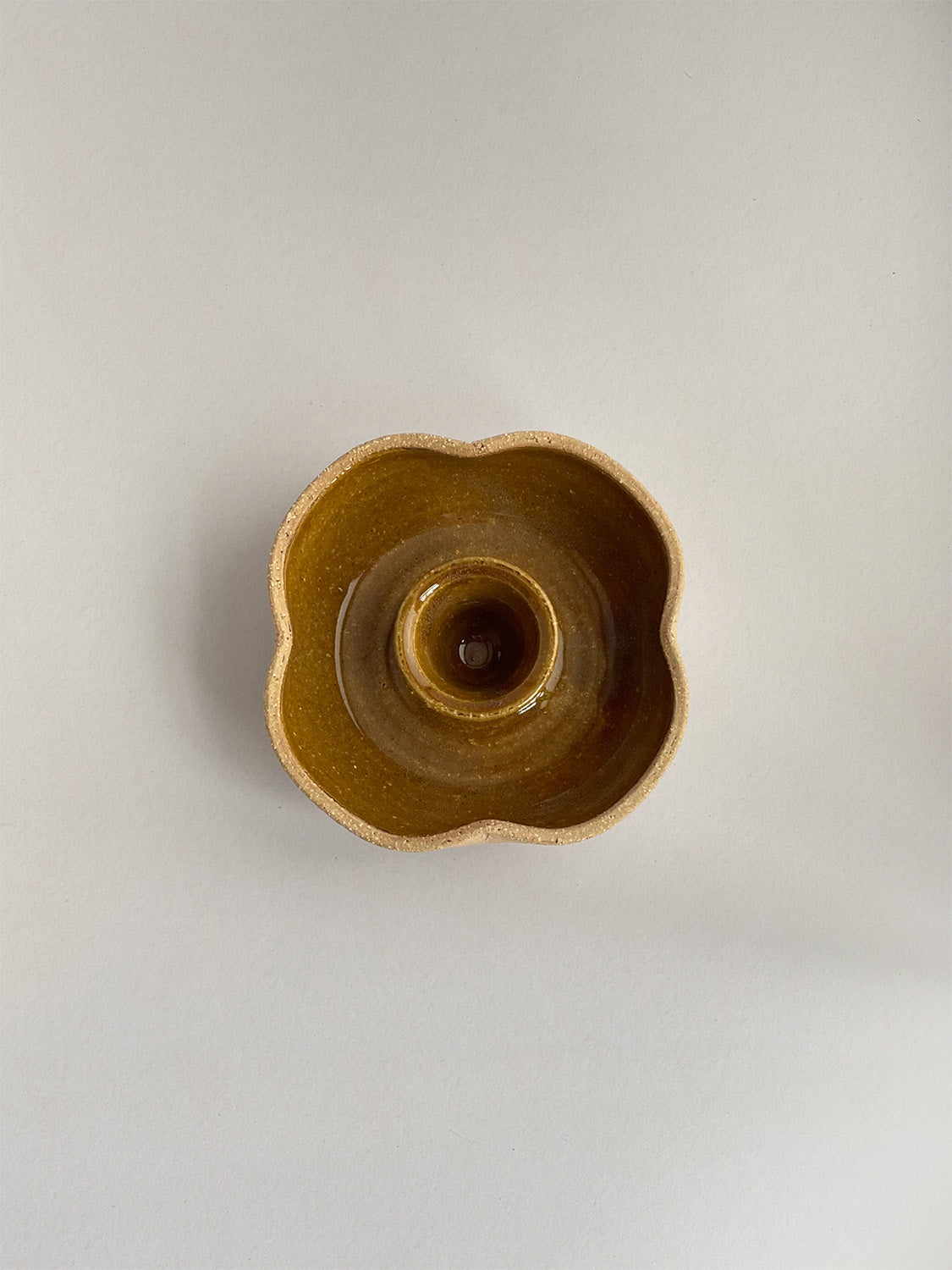 A hand-thrown ceramic candle holder in a rustic yellow ochre glaze on a neutral background - top view.