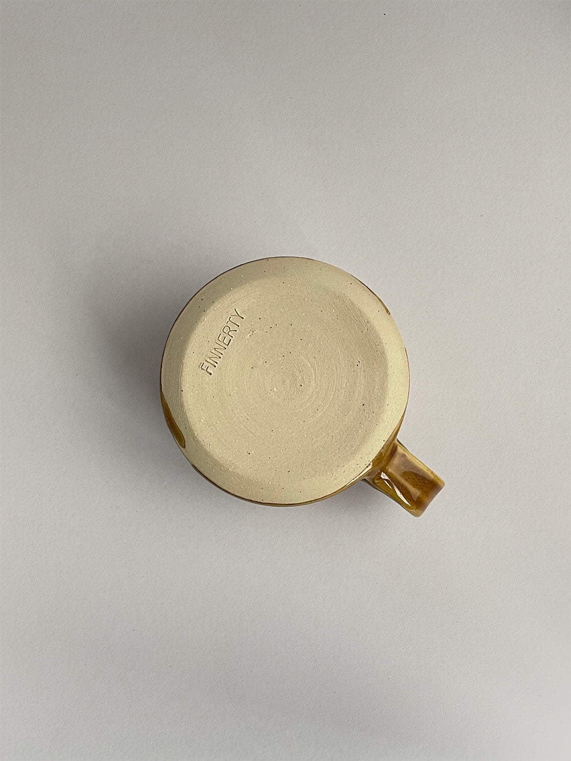 A golden yellow handmade ceramic espresso mug with a handle, on a neutral background - base view.