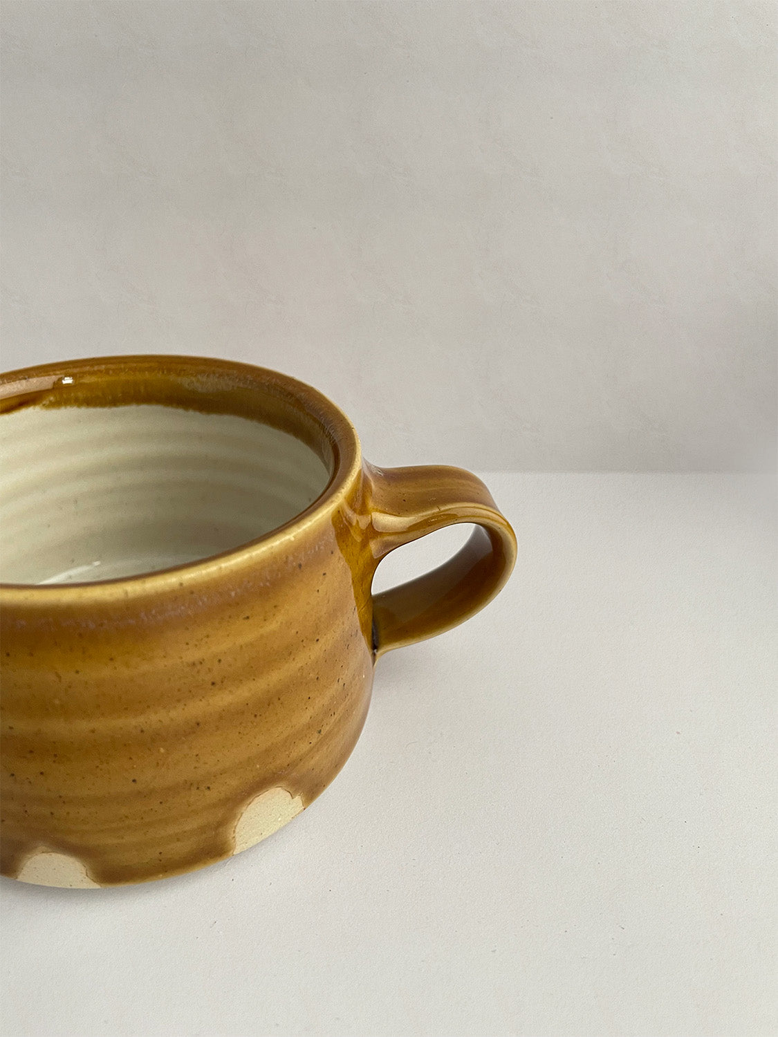 A golden yellow handmade ceramic espresso mug with a handle, on a neutral background - close-up view.