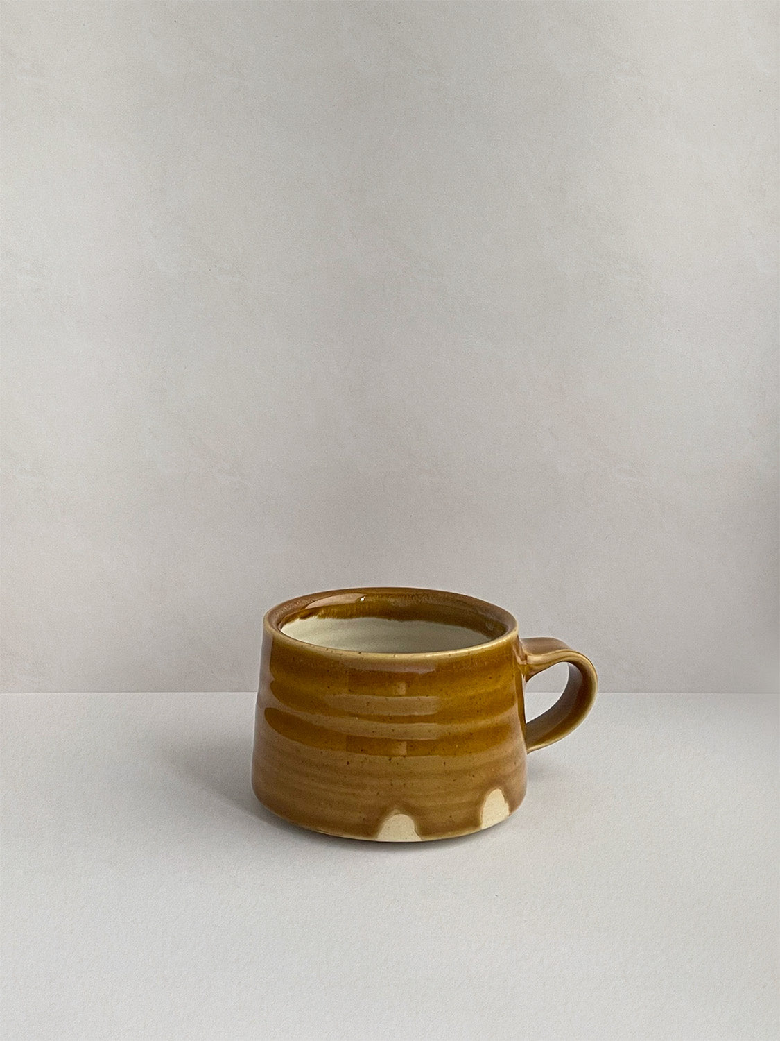 A golden yellow handmade ceramic espresso mug with a handle, on a neutral background - left side view.