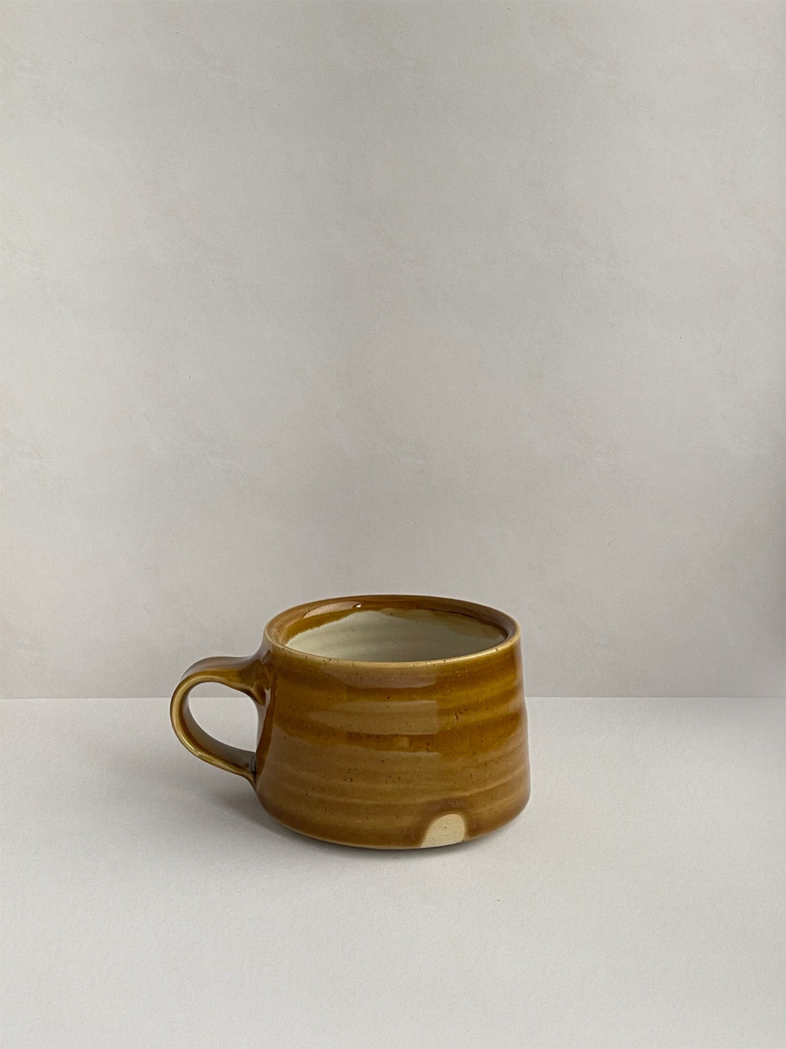 A golden yellow handmade ceramic espresso mug with a handle, on a neutral background - right side view.
