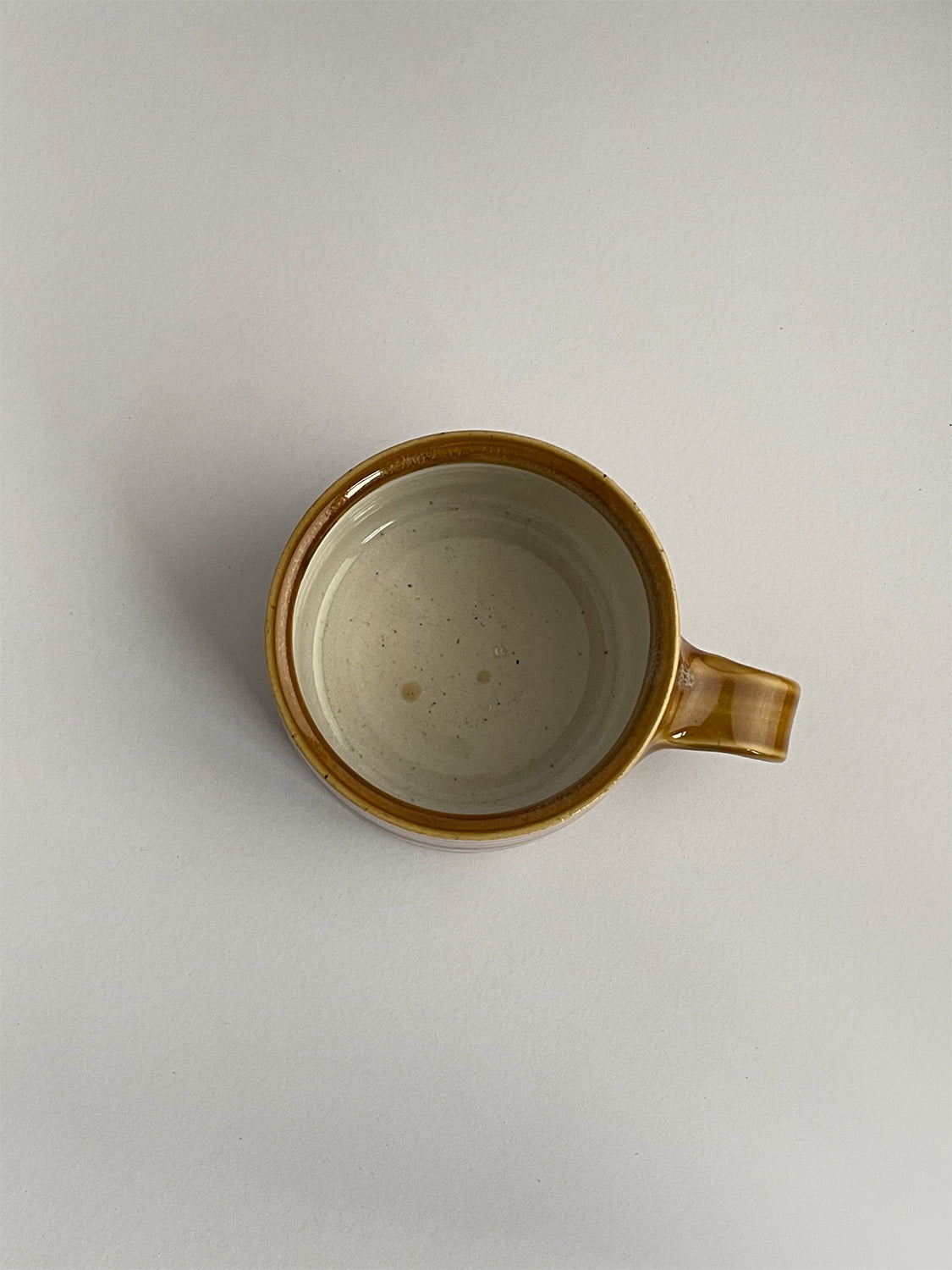 A golden yellow handmade ceramic espresso mug with a handle, on a neutral background - top view.