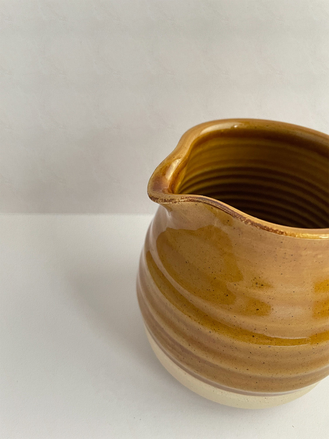 A golden yellow handmade ceramic jug with a curved body and a handle, on a neutral background - detail view.