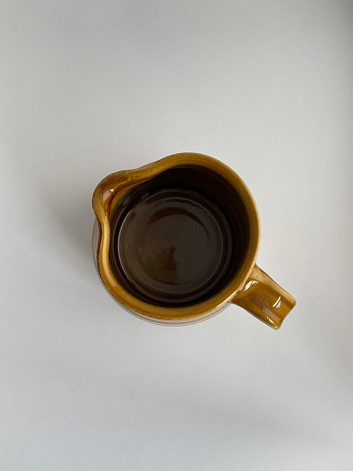 A golden yellow handmade ceramic jug with a curved body and a handle, on a neutral background - top view.