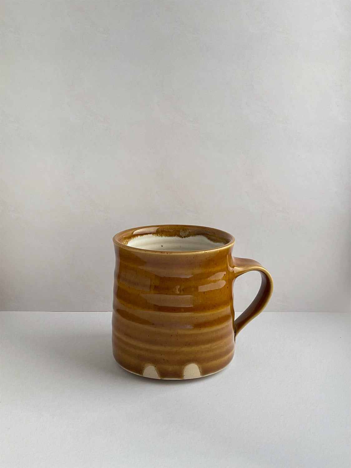 A hand-thrown ceramic mug with a handle, in a golden yellow glaze on a neutral background - left side view.