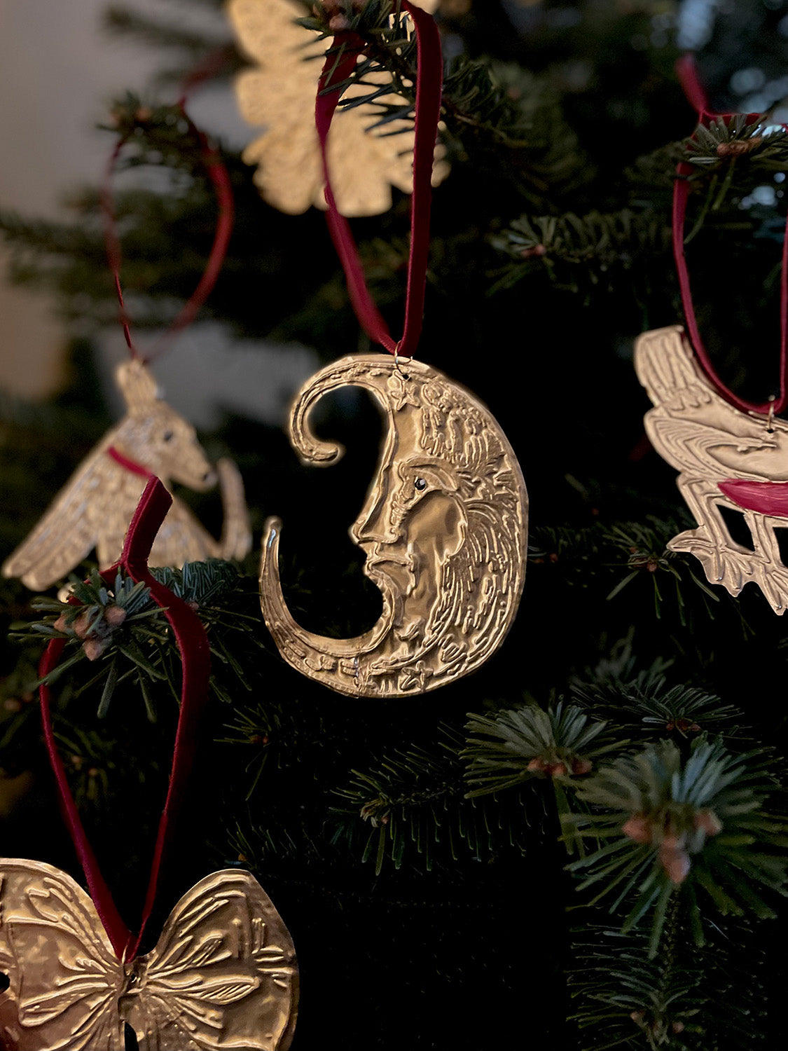 Handmade Christmas decorations featuring a gold metallic crescent moon ornament with red velvet ribbon on a festive tree.