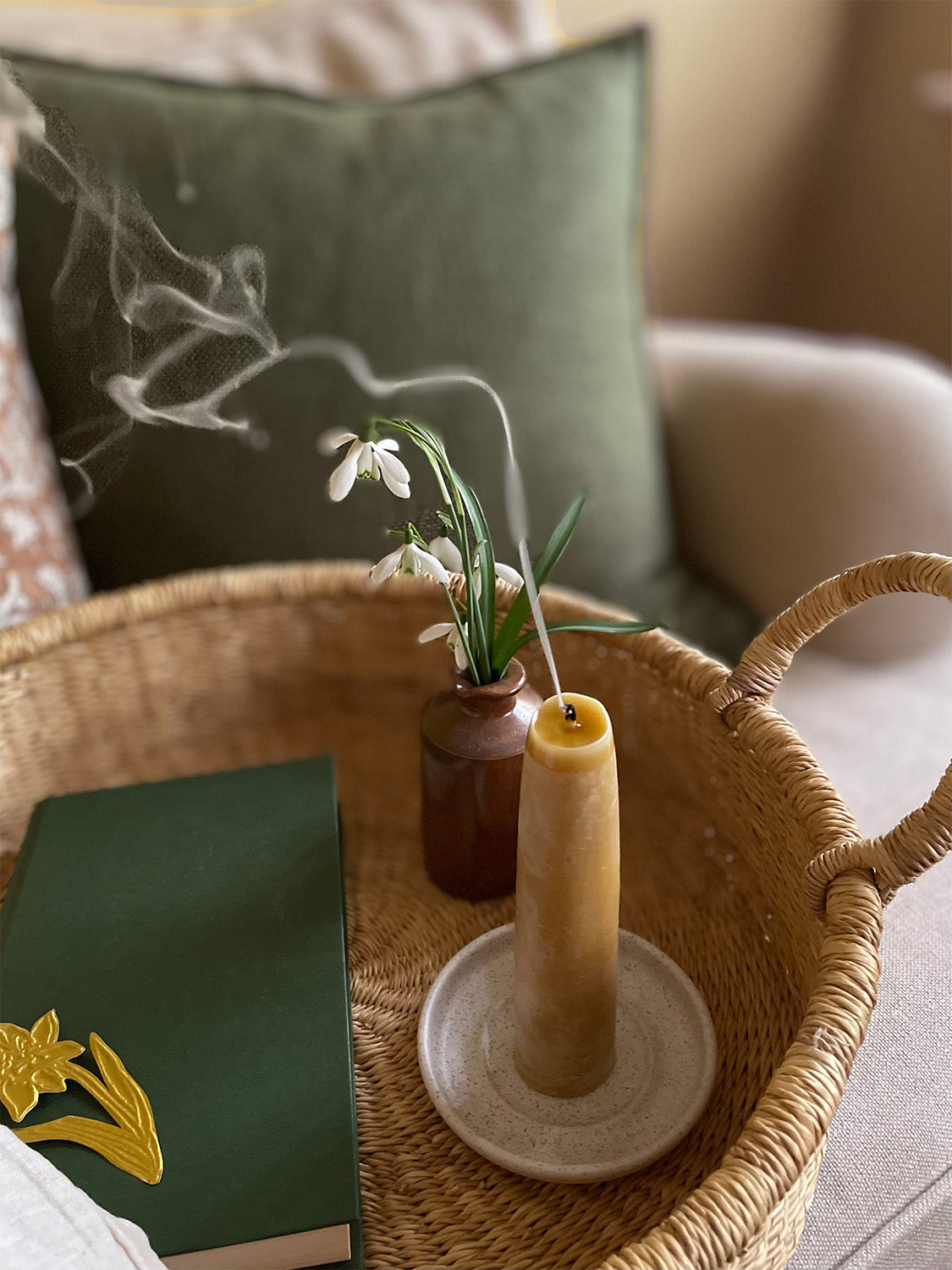 Natural beeswax candle with handmade holder displayed on a beautifully set table with flowers and bowls.