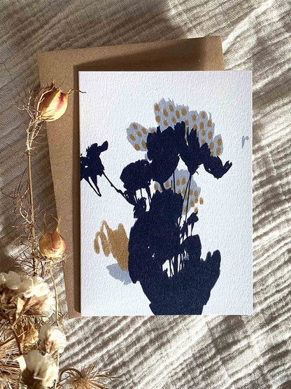 Autumn Shadows botanical greetings card with Kraft paper envelope on a cream, rippled fabric background with some dried flowers.