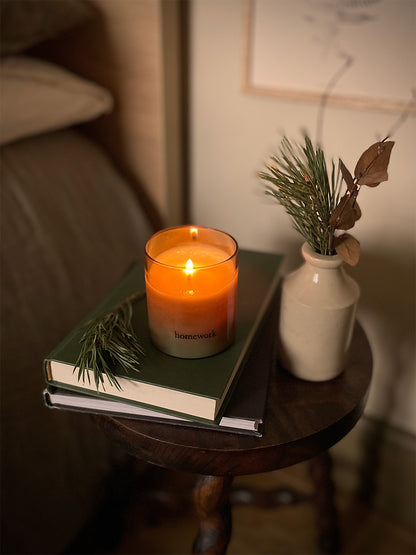 Candle on a stack of books with a vase of greenery on a bedside table in a cosy room.