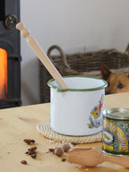 Enamel pot with beech wood porridge spurtle on a table near a can of syrup in a cosy kitchen setting.