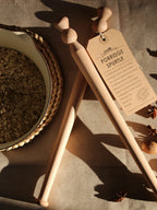 Two beech wood porridge spurtles  with a Kraft paper tag on a textured surface with a pan of oats.