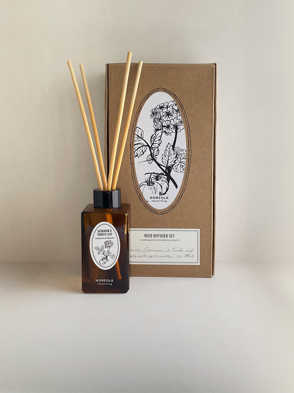 Geranium & Tomato Leaf botanical reed diffuser set with an amber glass bottle, natural wood reeds, and a brown kraft paper box featuring a black botanical illustration.