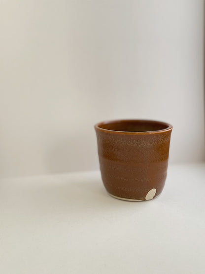 Burnt orange ceramic cup on a neutral background - detail view.