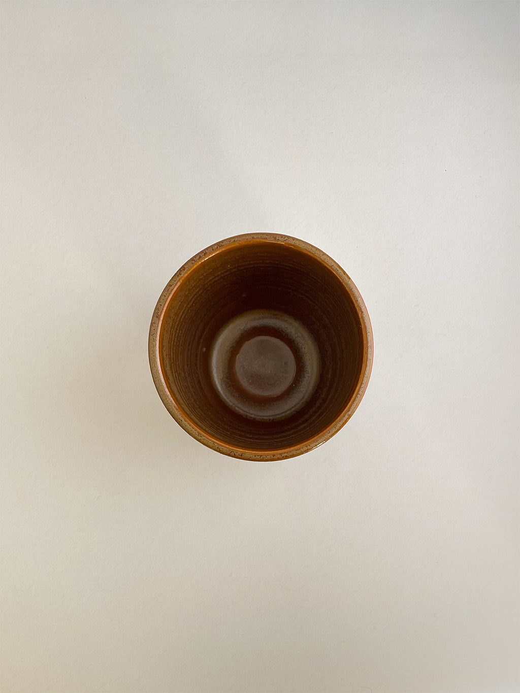 Burnt orange ceramic cup on a neutral background - top view.