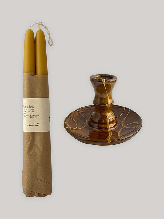 Pair of beeswax taper candles in brown paper packaging next to a ceramic candle holder squiggle patterns.