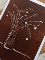 Close-up of a botanical Christmas card with a vase of festive foliage design on a dark red background.