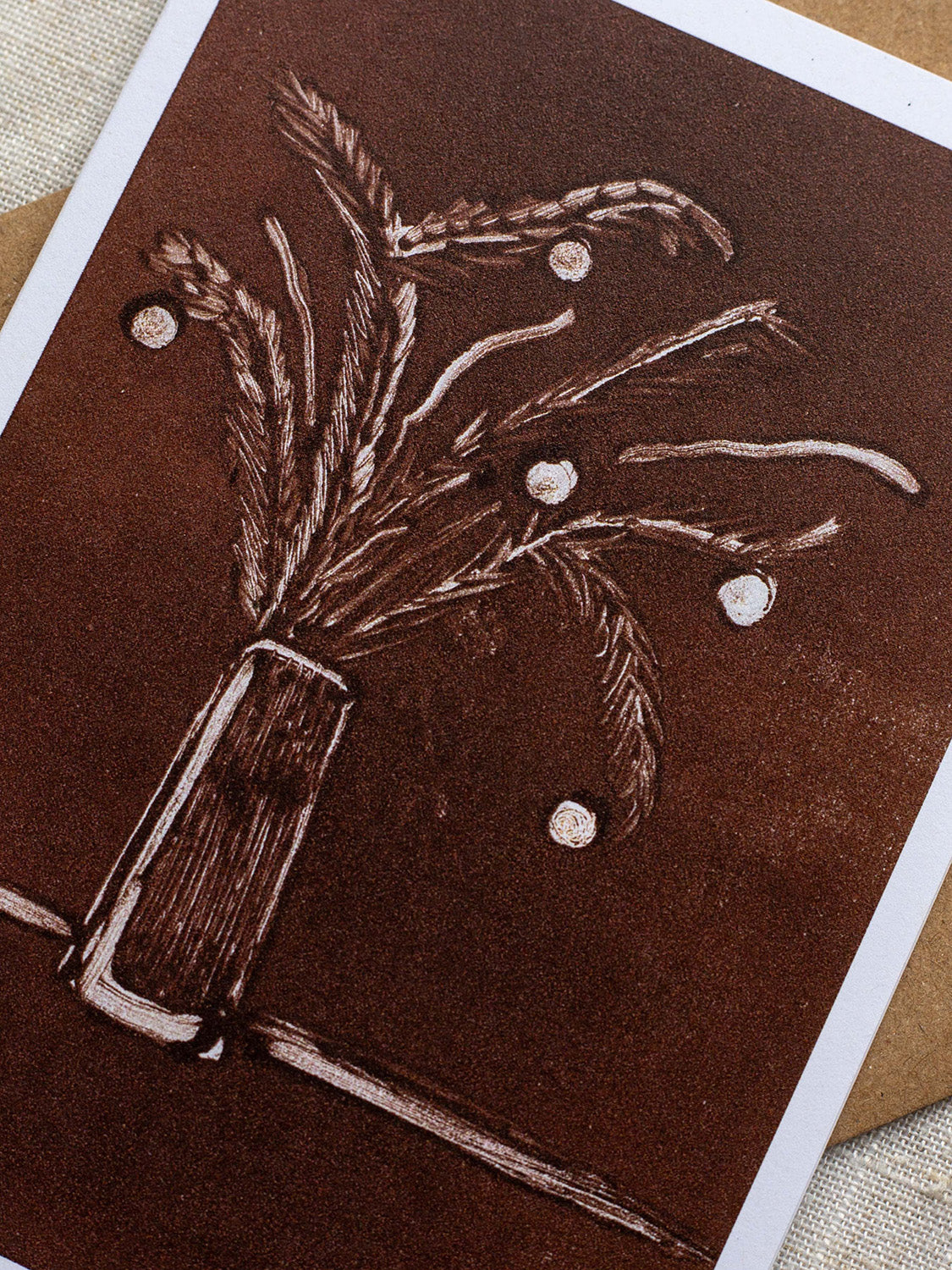 Close-up of a botanical Christmas card with a vase of festive foliage design on a dark red background.