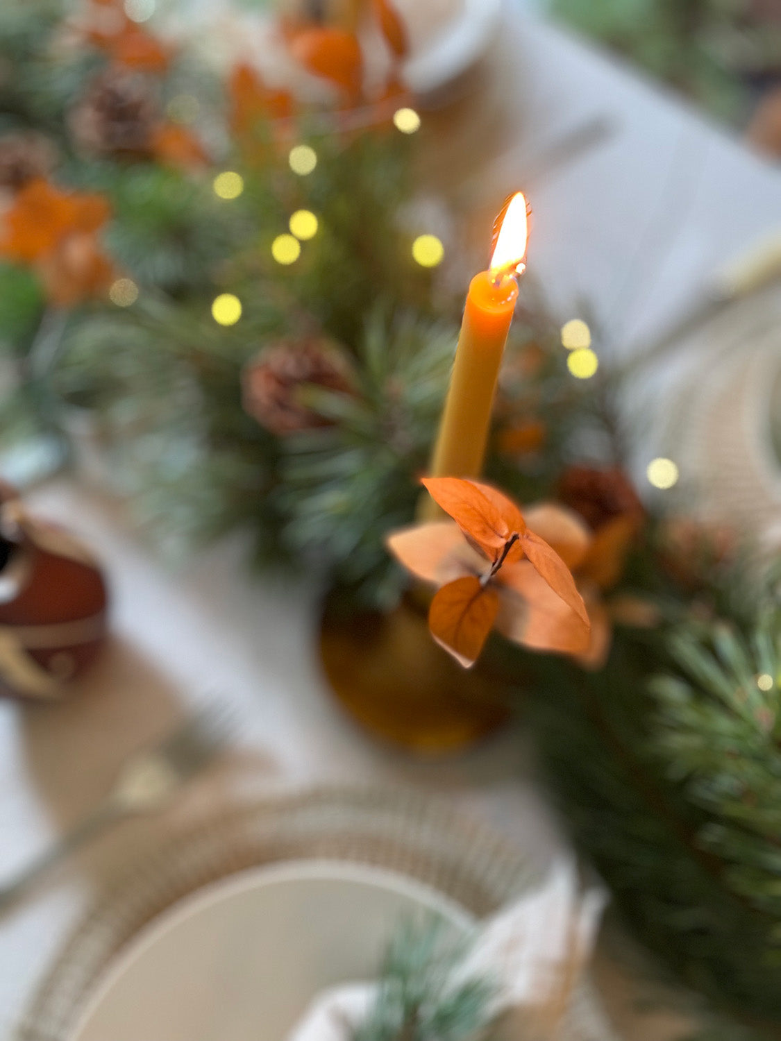 Lit beeswax taper candle on a decorative table with blurred background.