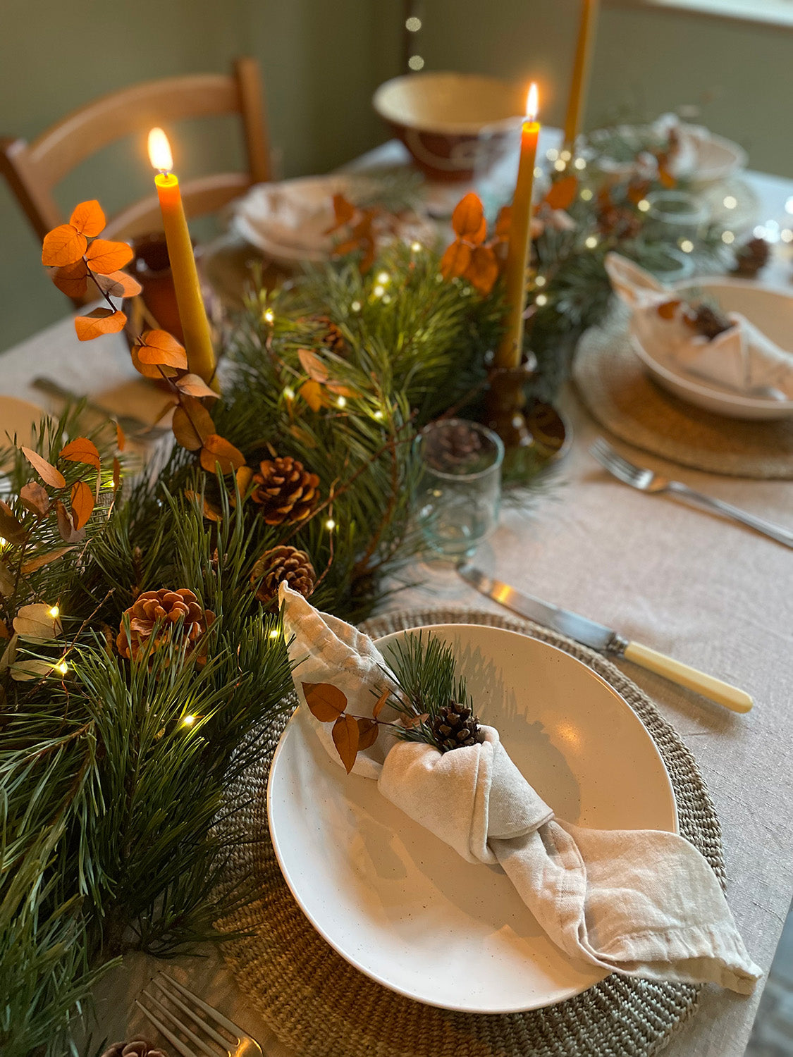 Decorative table setting with place settings, candles and festive greenery.