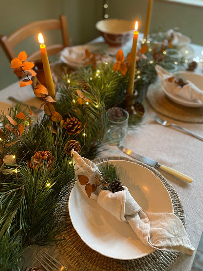 Decorative table setting with place settings, candles and festive greenery.