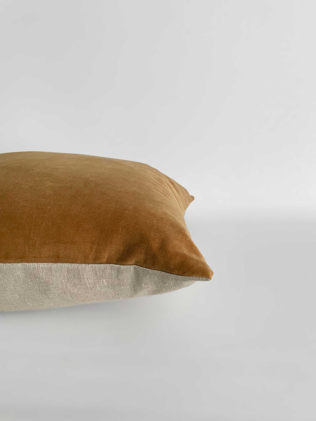 A square cushion with a warm caramel velvet top half and a light beige linen bottom half, against a clean, light neutral background.