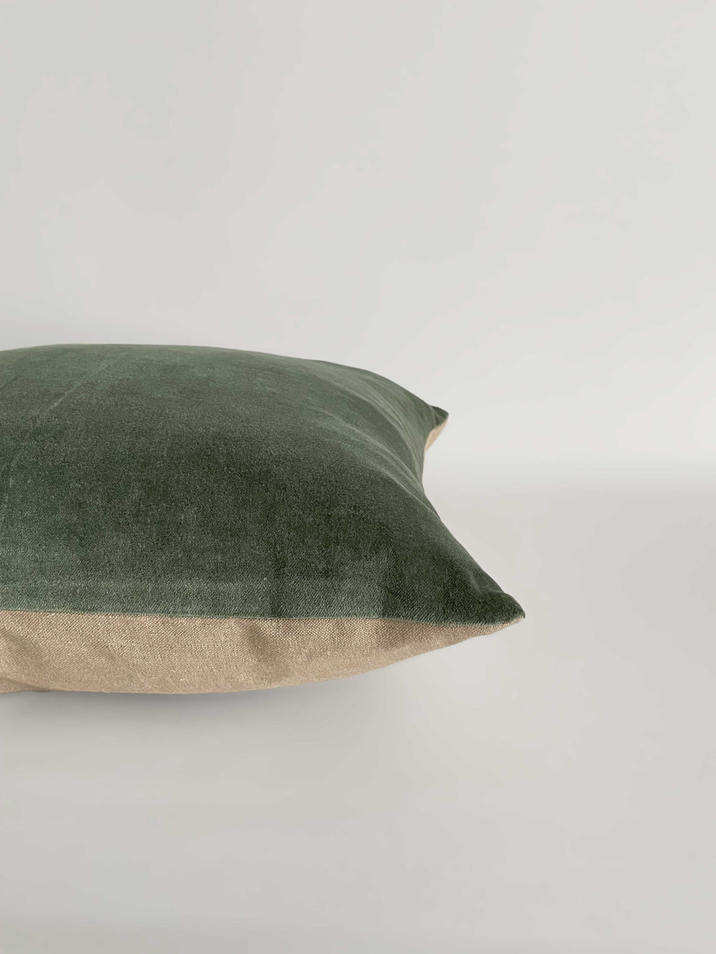 A square cushion with a sage green velvet top half and a light beige linen bottom half, against a clean, light neutral background.