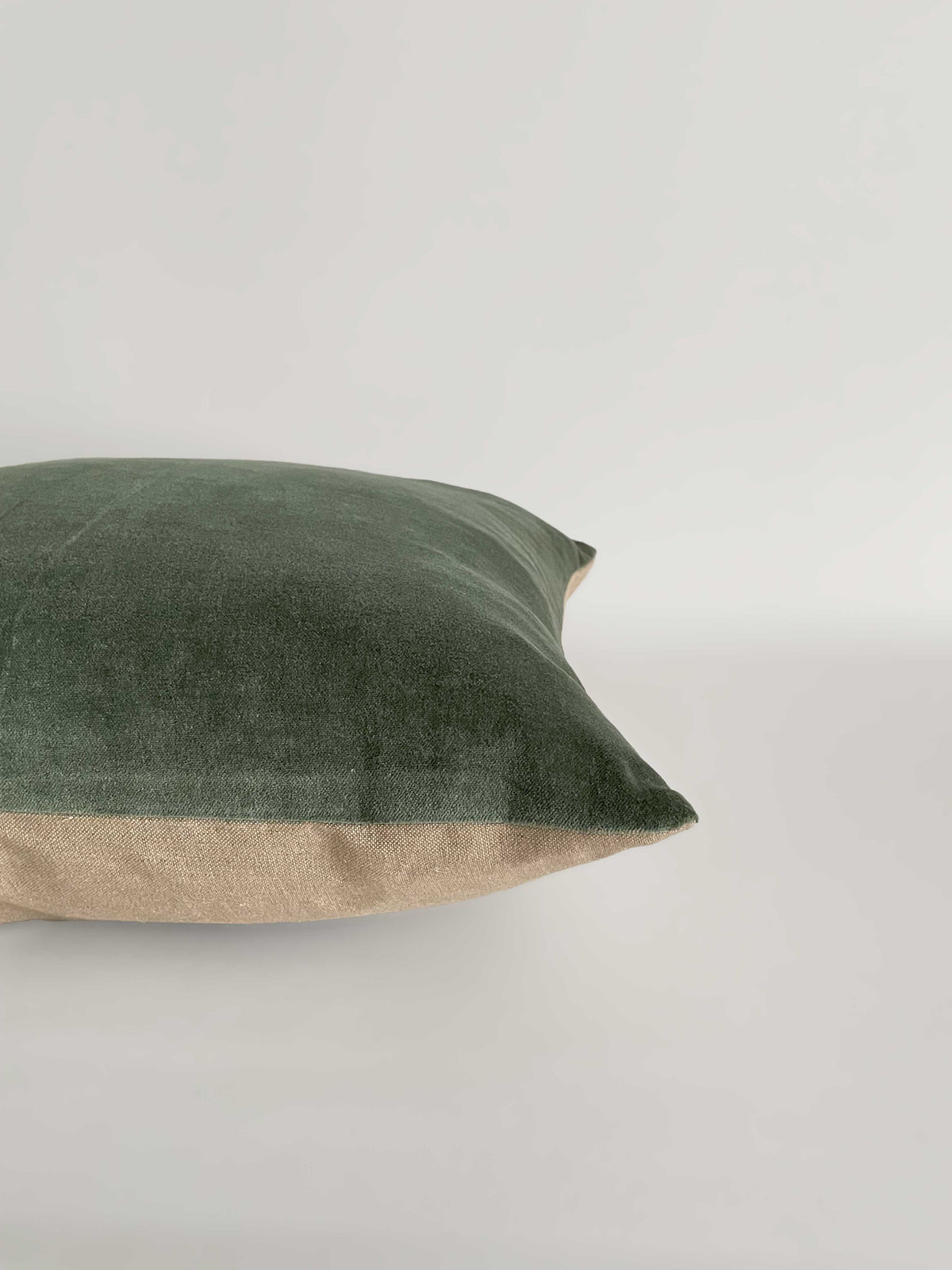 A square cushion with a sage green velvet top half and a light beige linen bottom half, against a clean, light neutral background.