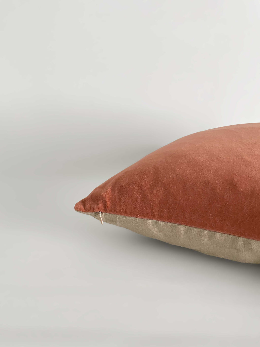 A square cushion with a terracotta velvet top half and a light beige linen bottom half, against a clean, light neutral background.