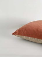 A square cushion with a terracotta velvet top half and a light beige linen bottom half, against a clean, light neutral background.