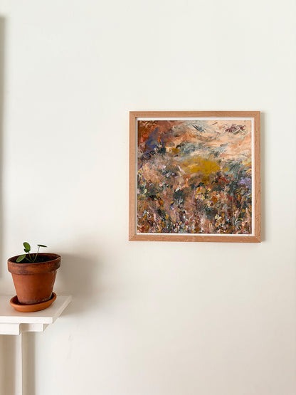 Abstract art print in a wooden frame on a white wall above a mantelpiece with a plant.