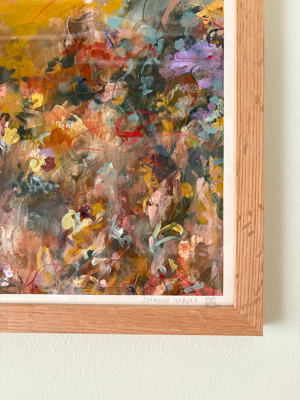 Close-up of abstract art print with warm, vibrant colours in a wooden frame on a white wall.