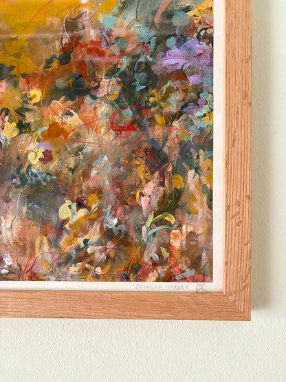Close-up of abstract art print with warm, vibrant colours in a wooden frame on a white wall.