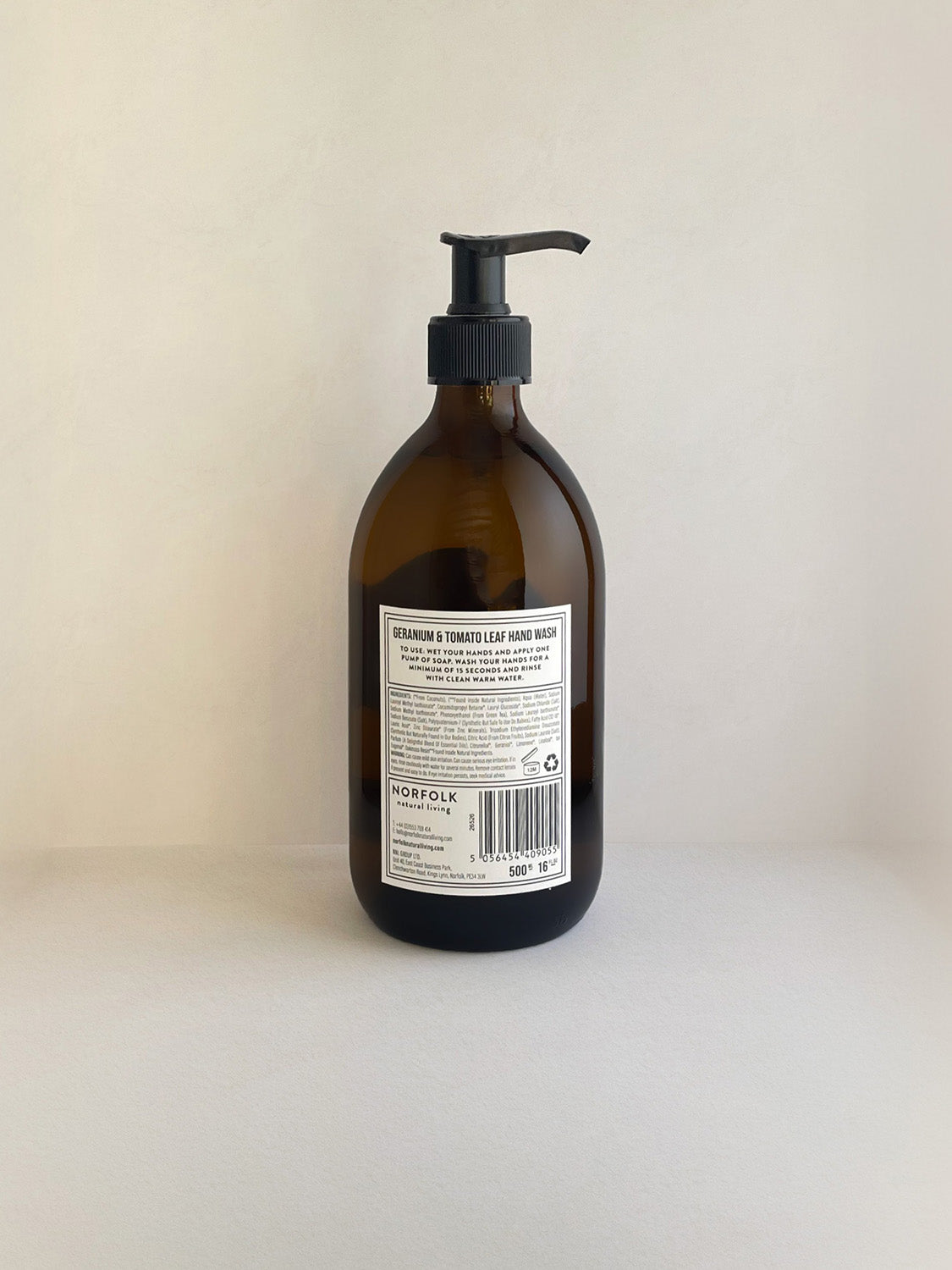 Geranium & Tomato Leaf hand wash in an amber glass bottle with pump and white label shown from the back, on a neutral background.