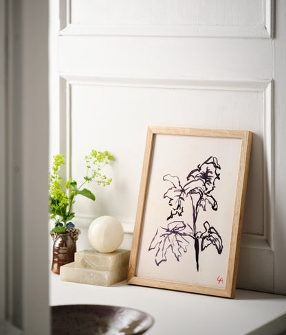 Art print of Geranium leaves in dark brown ink on vintage paper in a natural oak frame, sitting on a white painted windowsill alongside three alabaster ornaments and a brown stoneware vessel with wildflowers