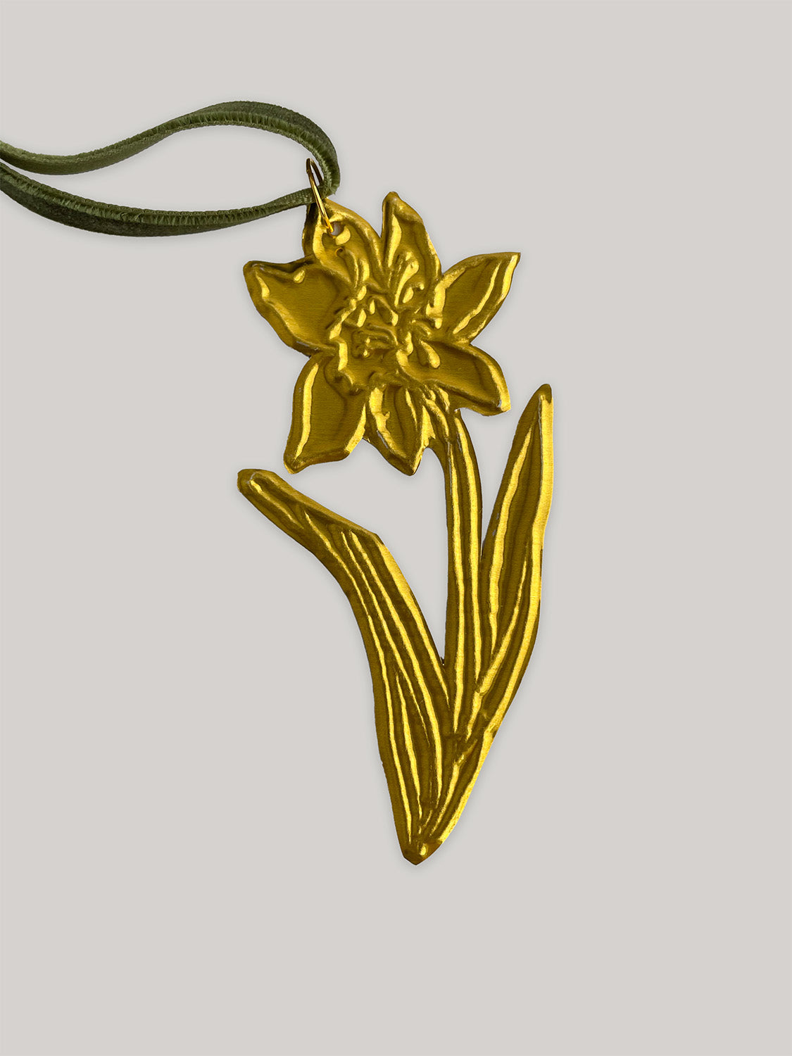 Gold tin daffodil handmade ornament with green velvet ribbon on a neutral background - close-up detail.