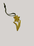 Gold tin daffodil handmade ornament with green velvet ribbon on a neutral background - front.
