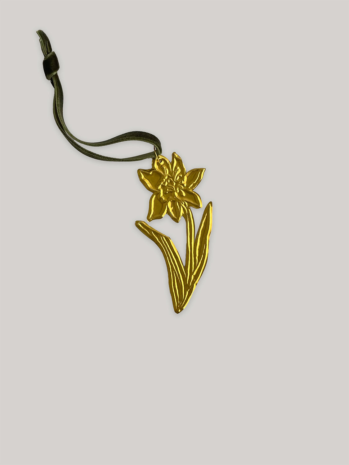 Gold tin daffodil handmade ornament with green velvet ribbon on a neutral background - front.