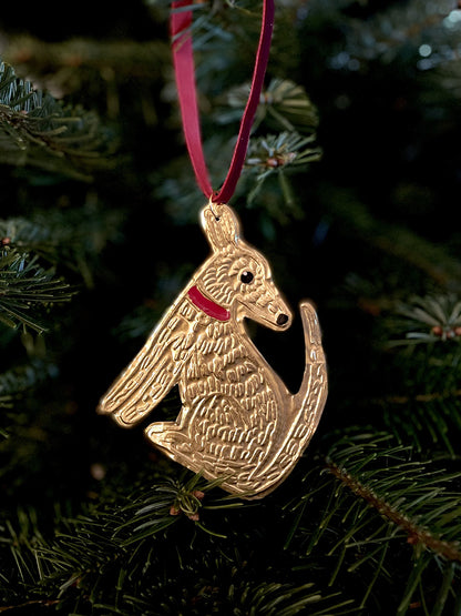 Gold dog-shaped Christmas ornament on a red ribbon against a green tree background.