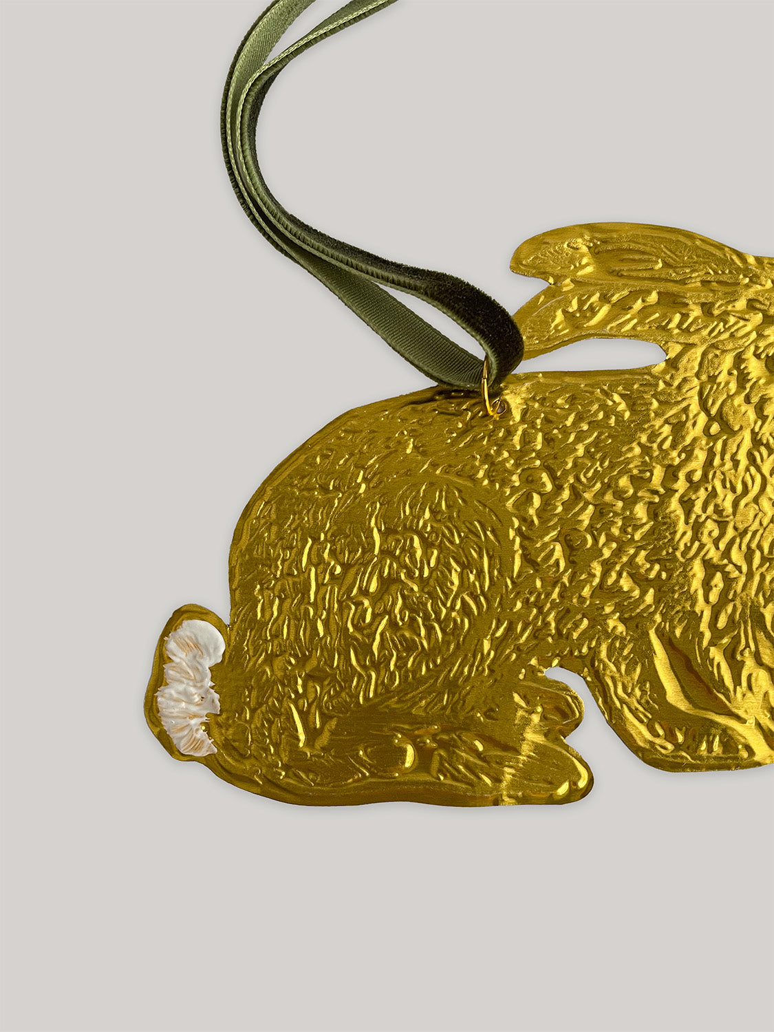 Gold tin hare handmade ornament with green velvet ribbon on a neutral background - close-up detail 1.
