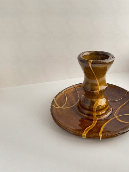 Close-up view of brown and gold handmade ceramic candle holder with decorative patterns on a neutral background.